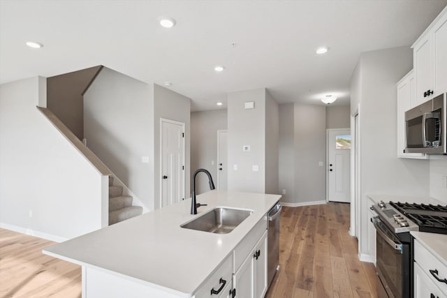 kitchen with sink, stainless steel appliances, an island with sink, and white cabinetry