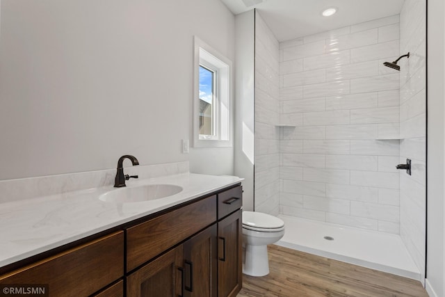 bathroom with tiled shower, toilet, vanity, and wood finished floors