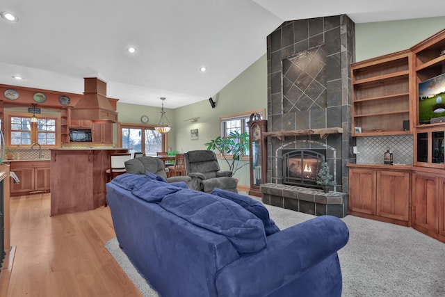 living room featuring high vaulted ceiling, sink, a fireplace, and light hardwood / wood-style flooring