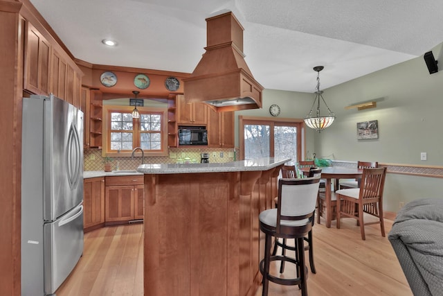 kitchen with hanging light fixtures, stainless steel fridge, a kitchen breakfast bar, and light hardwood / wood-style floors