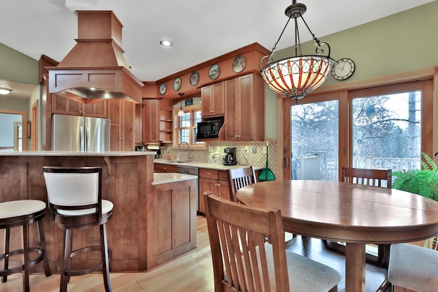 kitchen with sink, light wood-type flooring, pendant lighting, stainless steel appliances, and backsplash