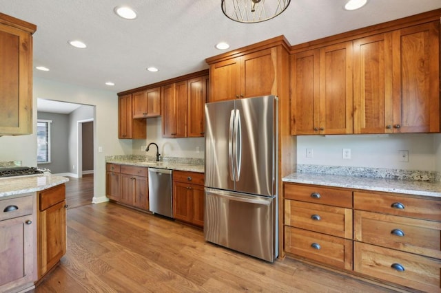 kitchen with light stone counters, light wood-type flooring, sink, and appliances with stainless steel finishes