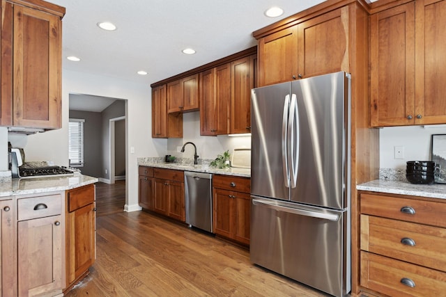 kitchen featuring appliances with stainless steel finishes, sink, light stone counters, and light hardwood / wood-style floors