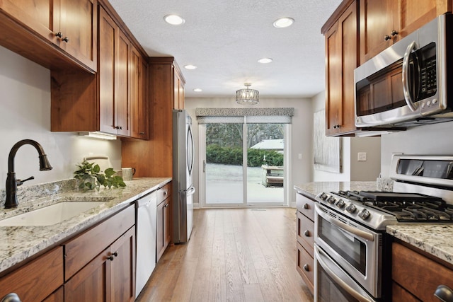 kitchen featuring stainless steel appliances, light stone countertops, sink, and light hardwood / wood-style flooring