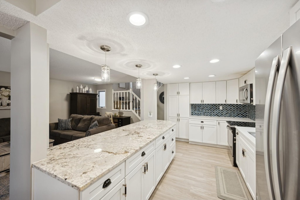 kitchen featuring decorative light fixtures, white cabinetry, stainless steel appliances, backsplash, and light stone counters