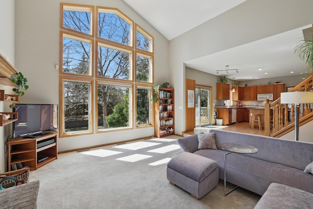living area with high vaulted ceiling, plenty of natural light, stairway, and light carpet