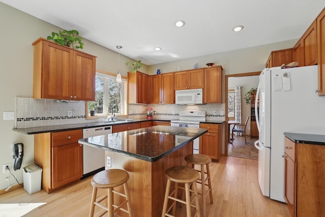 kitchen featuring brown cabinets, light wood-type flooring, a breakfast bar, and white appliances