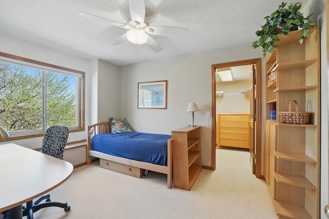 bedroom featuring a walk in closet, a ceiling fan, a textured ceiling, light colored carpet, and a closet
