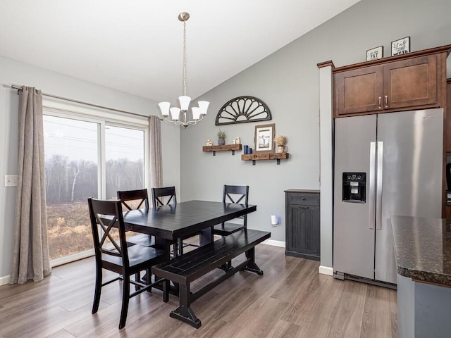 dining area featuring a chandelier, light hardwood / wood-style floors, and vaulted ceiling