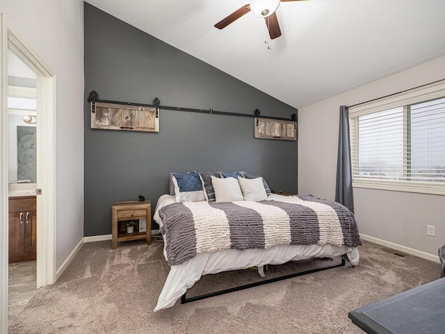 carpeted bedroom featuring a barn door, ceiling fan, ensuite bathroom, and vaulted ceiling