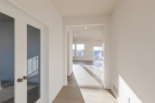 corridor with light hardwood / wood-style floors and french doors