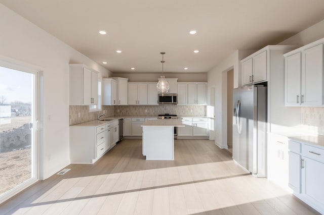 kitchen featuring sink, a center island, decorative light fixtures, white cabinets, and appliances with stainless steel finishes