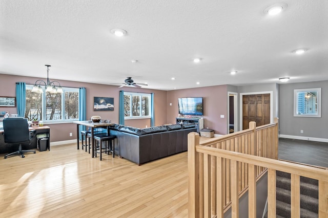 living room with ceiling fan with notable chandelier, a textured ceiling, and light hardwood / wood-style flooring