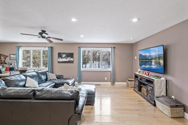 living room with ceiling fan, a textured ceiling, and light wood-type flooring