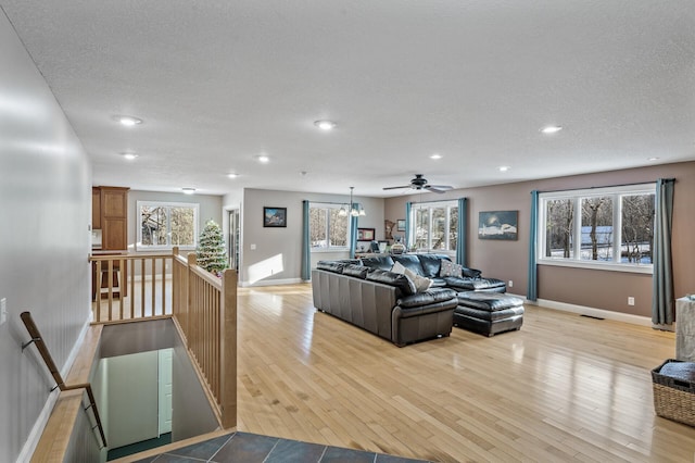 living room featuring ceiling fan with notable chandelier, a textured ceiling, and light hardwood / wood-style floors