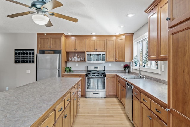 kitchen with ceiling fan, sink, stainless steel appliances, and light hardwood / wood-style floors