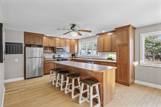 kitchen with appliances with stainless steel finishes, a kitchen breakfast bar, ceiling fan, sink, and a center island