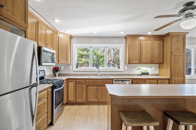 kitchen with ceiling fan, sink, a kitchen breakfast bar, appliances with stainless steel finishes, and light wood-type flooring