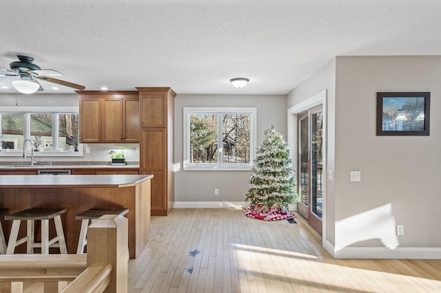 kitchen with ceiling fan, sink, light hardwood / wood-style flooring, a textured ceiling, and a kitchen bar