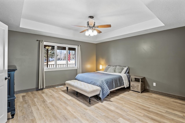 bedroom with a tray ceiling, ceiling fan, and light wood-type flooring