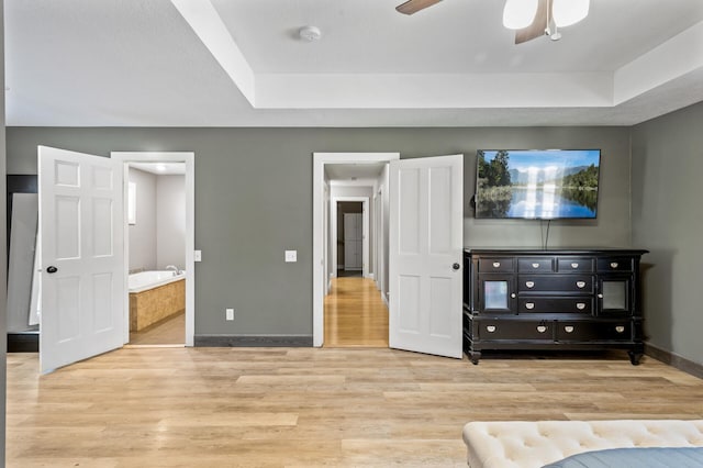 unfurnished bedroom with connected bathroom, a tray ceiling, light hardwood / wood-style flooring, and ceiling fan