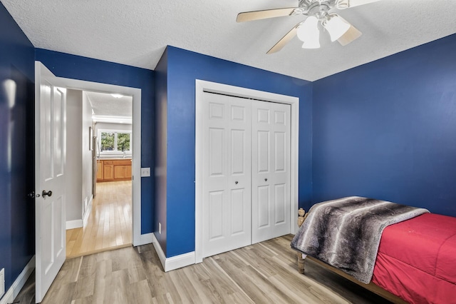 bedroom with ceiling fan, light hardwood / wood-style floors, a textured ceiling, and a closet