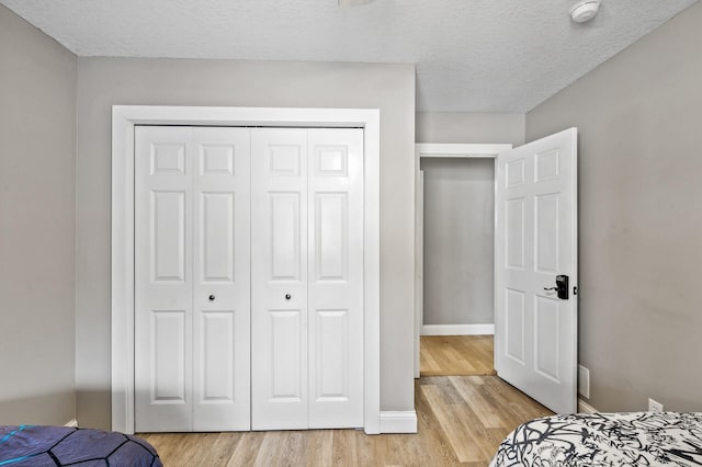 bedroom with a textured ceiling, light wood-type flooring, and a closet