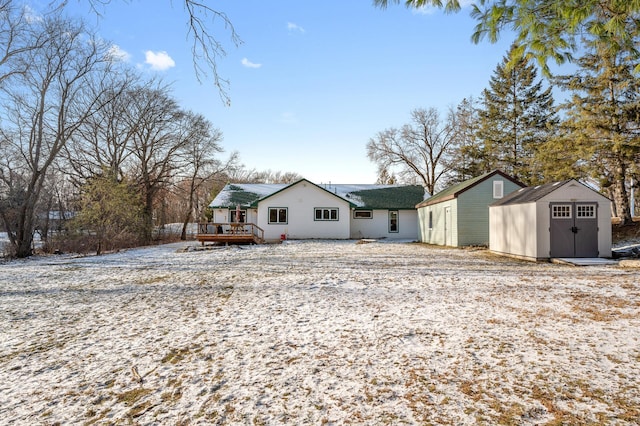 snow covered back of property featuring a deck and a storage shed