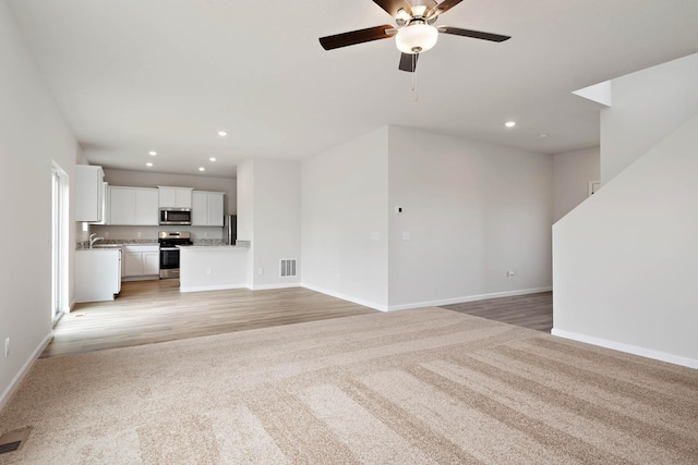 unfurnished living room featuring ceiling fan, light wood-type flooring, and sink