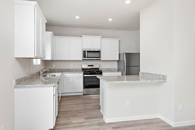 kitchen featuring sink, light stone countertops, appliances with stainless steel finishes, light hardwood / wood-style floors, and white cabinetry