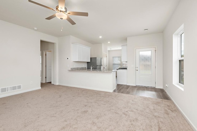 kitchen with kitchen peninsula, stainless steel fridge, white cabinetry, and light stone countertops