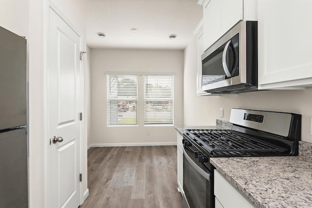 kitchen featuring light stone countertops, white cabinets, stainless steel appliances, and light hardwood / wood-style floors