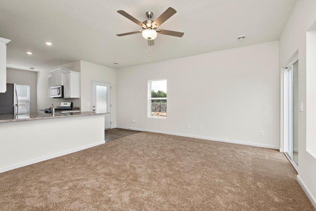 unfurnished living room featuring ceiling fan, sink, and dark carpet