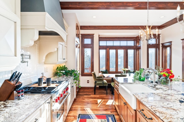 kitchen featuring sink, an inviting chandelier, high end stove, backsplash, and pendant lighting