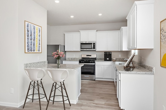 kitchen with stainless steel appliances, a peninsula, a sink, white cabinets, and a kitchen bar