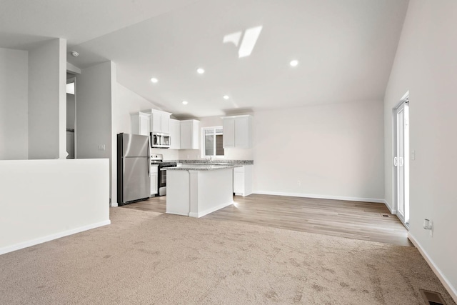 kitchen with light stone countertops, appliances with stainless steel finishes, white cabinetry, a kitchen island, and lofted ceiling