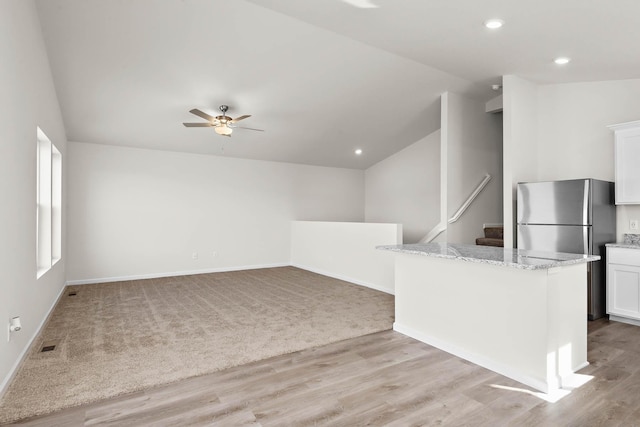 kitchen featuring light hardwood / wood-style floors, white cabinetry, lofted ceiling, and light stone counters