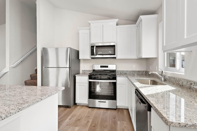 kitchen with stainless steel appliances, white cabinetry, lofted ceiling, and light hardwood / wood-style floors