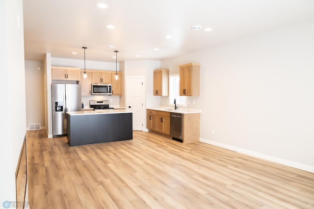 kitchen featuring sink, hanging light fixtures, stainless steel appliances, a kitchen island, and light wood-type flooring