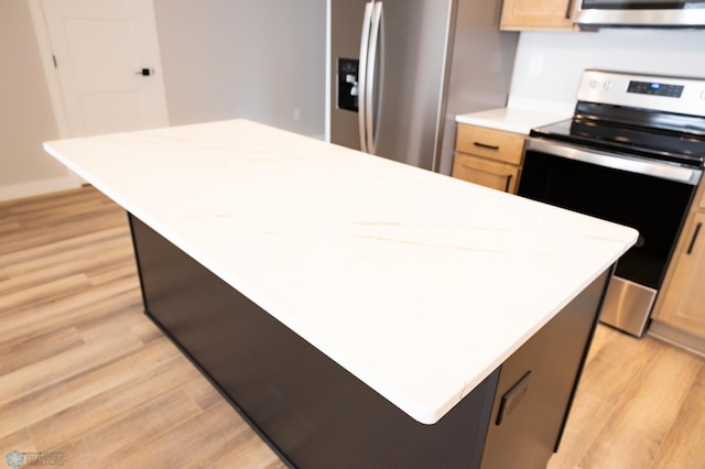 kitchen featuring light wood-type flooring, appliances with stainless steel finishes, light brown cabinets, and a kitchen island