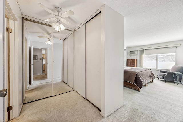 bedroom with a textured ceiling, a wall unit AC, a closet, ceiling fan, and light carpet