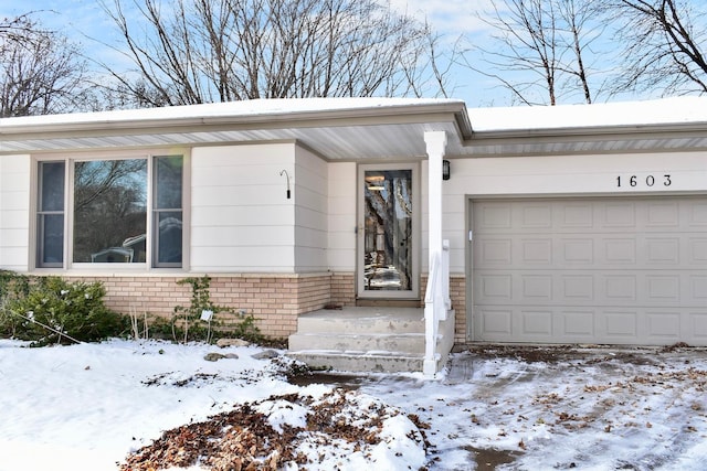 snow covered property entrance with a garage