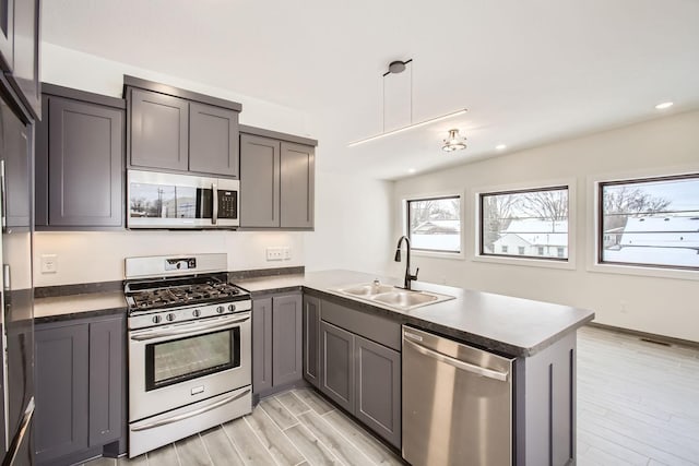 kitchen featuring kitchen peninsula, sink, hanging light fixtures, light wood-type flooring, and appliances with stainless steel finishes