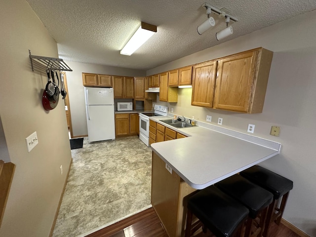 kitchen with kitchen peninsula, a kitchen breakfast bar, white appliances, a textured ceiling, and sink