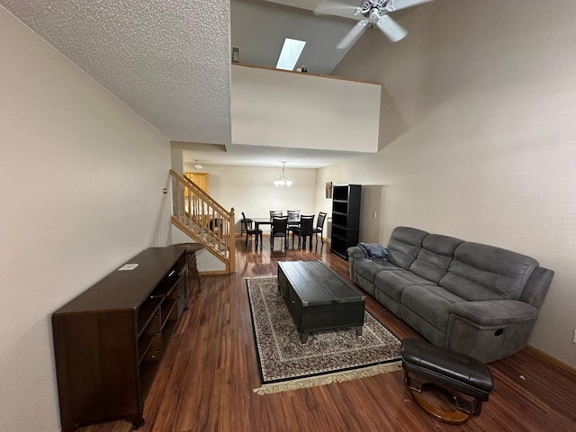 living room featuring dark wood-type flooring, a high ceiling, ceiling fan with notable chandelier, a skylight, and a textured ceiling