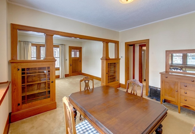 carpeted dining room with ornamental molding, a textured ceiling, and decorative columns