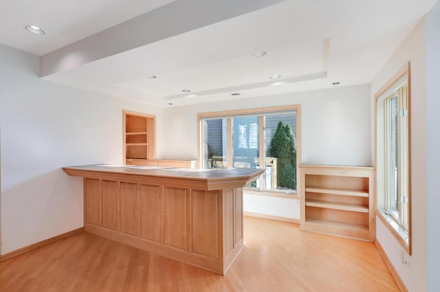 kitchen with light wood-type flooring, a tray ceiling, a peninsula, and tile counters