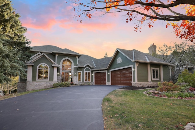 view of front of property featuring a garage, stone siding, driveway, and a lawn