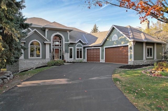 view of front facade featuring a garage, a shingled roof, stone siding, aphalt driveway, and a front lawn