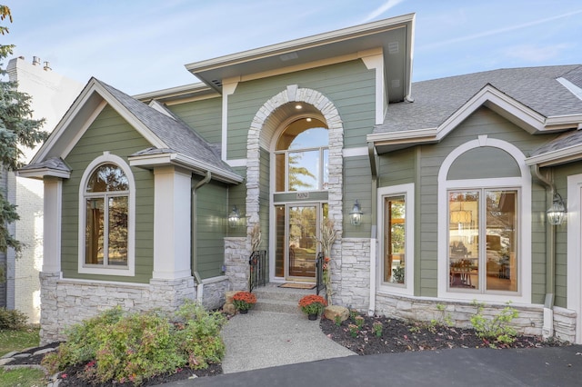 view of exterior entry featuring stone siding and roof with shingles